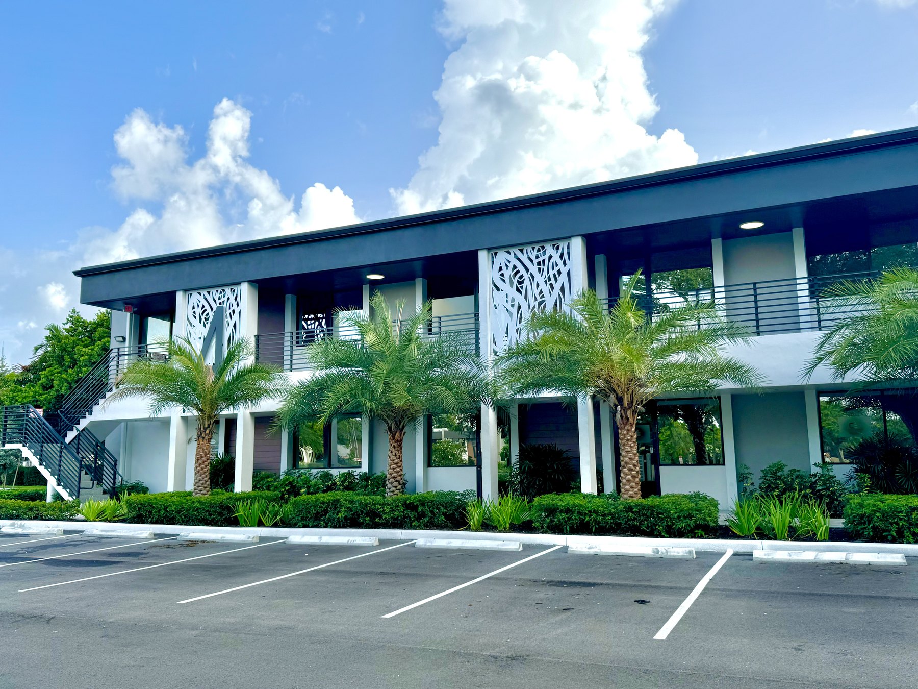 Sunlit office building exterior with queen palms and open parking at the park